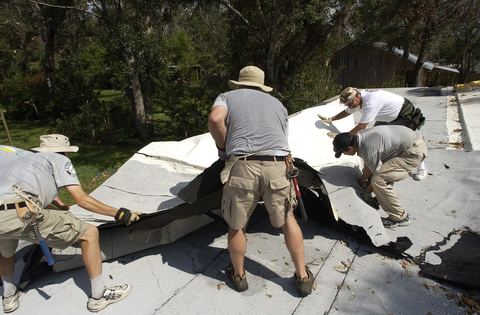 Workers peeling a worn white membrane off a low-slope roof during a repair