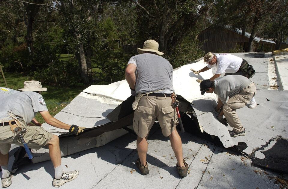 Workers peeling a worn white membrane off a low-slope roof during a repair