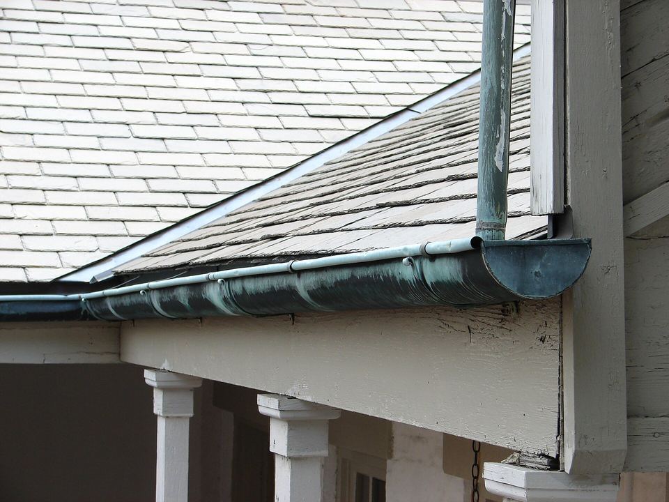 Copper half-round gutter and downspout along the porch eave of an old wooden house