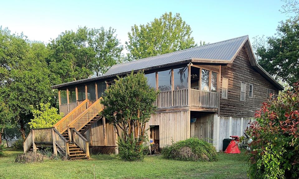 Raised wooden cottage with a gray standing-seam metal roof, screened porch and outside stairs