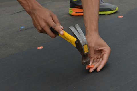 Hands hammering a plastic cap nail into dark roof underlayment